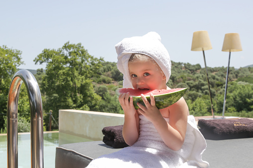 Toddler girl wrapped in bath towel eating watermelon
