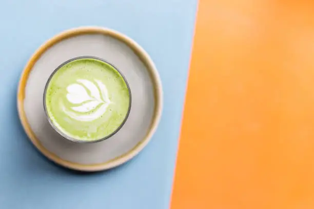 Top view of a matcha latte on a light blue and orange background.