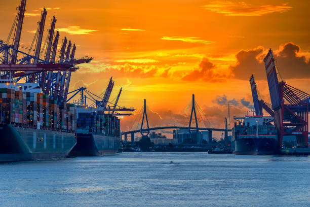 Harbor and a bridge in the morning Container ships, harbor cranes and a bridge in the far. Orange, morning sky in background. Small motorboat passing the dock. köhlbrandbrücke stock pictures, royalty-free photos & images