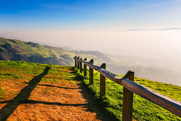 Picturesque green hills, pasture and hiking trail with wooden fence in sunlight. Scenic countryside in mountains at sunset. Colorful landscape in California, USA. Alum Rock Park.