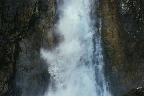 istock Atmospheric minimal landscape with vertical big waterfall on rock mountain wall. Powerful large waterfall in dark gorge. Nature background of high vertical turbulent falling water stream on wet rocks. 1335500006
