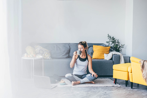 Woman sitting and drinking coffee after workout session at home.