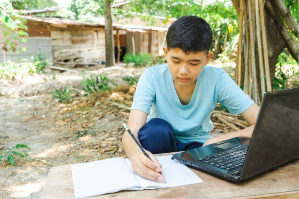 istock A boy is writing in a notebook while studying online with a laptop computer at home in the countryside 1335512763
