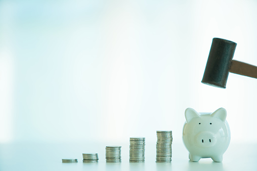 Unrecognizable Asian young woman using a metal hammer to smash down the piggy bank on the table. Woman tear down the piggy saving by using hammer.