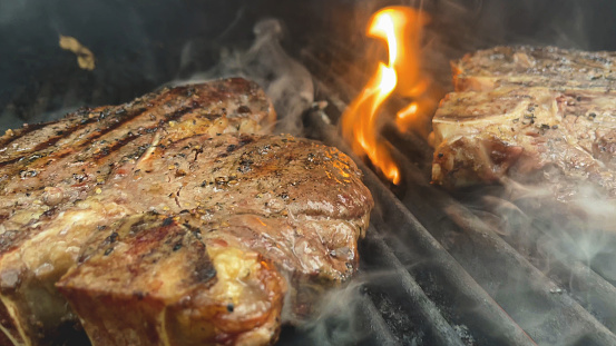 Flame Grilled Prime Ribeye Steaks on BBQ Cooking Grill with Smoke and Flames Matching 4K Video Available (Shot with iPhone 12 Pro Max Video Screen Grab photos professionally retouched - Lightroom / Photoshop -downsampled as needed for clarity and select focus used for dramatic effect)