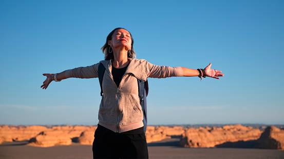 asian backpacker female tourist enjoying nature with arms outstretched eyes closed