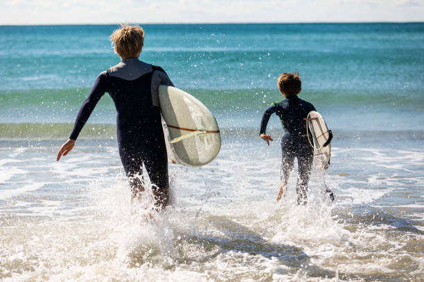 surf padre e figlio corrono in acqua insieme - surfing beach family father foto e immagini stock