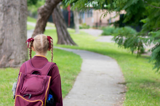 一人で学校に歩いて行くマルーンの制服を着た女の子。学校の生徒はcovid-19の流行後に教室に戻ります - australian culture 写真 ストックフォトと画像