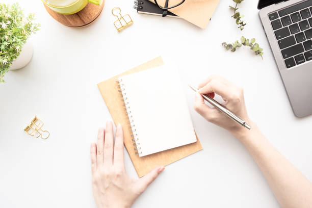istock Business woman is going to write something on blank notebook over white office desk table, top view. 1335531559