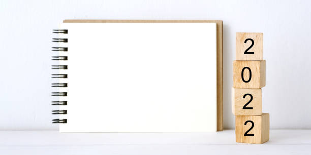 istock 2022 on wood block, blank notebook paper on white table background, 2022 new year mock up, template with copy space for text 1335532477