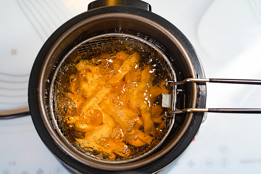 top view. oil boiling in a deep fryer. in the basket of the fryer cook shrimp in batter or potatoes. gadgets for the kitchen. cooking in boiling vegetable oil.