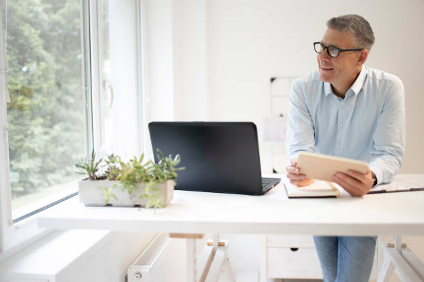 istock man with blue shirt and black glasses is standing behind standing table and is working with his tablet 1335540201