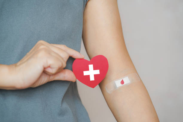 世界の献血とドナーの日のための包帯に赤い紙の心臓の形と赤い血滴シ��ンボルを保持し、命の概念を救うシニア人間の手 - blood ストックフォトと画像