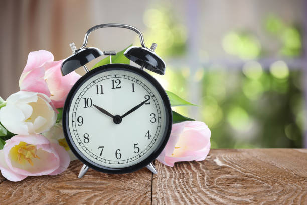istock Alarm clock and flowers on table against blurred background. Spring time 1335544872