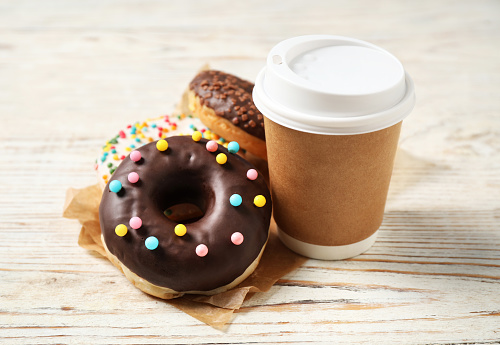 Delicious glazed donuts and coffee on white wooden table