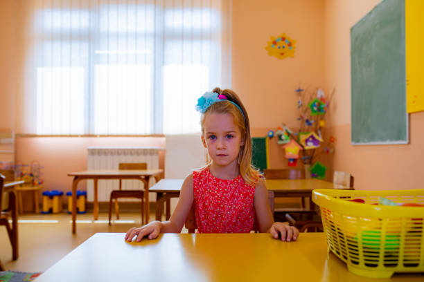 Sad ad serious preschool girl, refusing to play in the classroom with a toy blocks