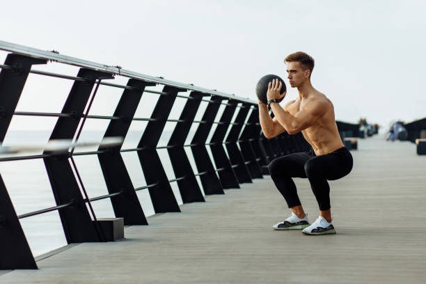 istock Sporty man without t-shirt doing exercises with ball, Man doing workout using medicine ball outdoors on pier 1335547160