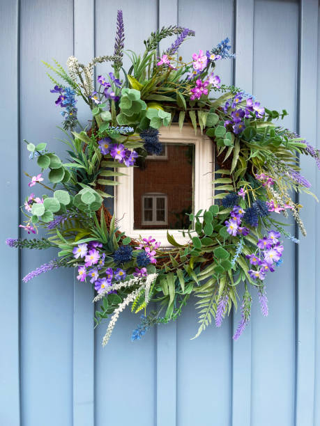 Close-up image of light blue, wood panelled front door with look out window and Summer wreath decoration with purple, silk flowers and plastic, green foliage Stock photo showing a light blue, front door with an artificial, summer wreath decoration of green foliage and purple flowers including eucalyptus and fern leaves with purple lavender, violets and daisies. door panel stock pictures, royalty-free photos & images