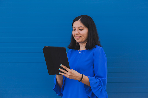Young beautiful woman with blue shirt working with a digital tablet, posing over blue background.