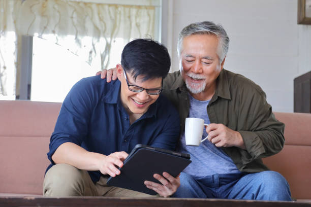 homme asiatique senior en âge de prendre sa retraite en regardant la photo du produit disponible en ligne dans la tablette numérique de son fils - generation gap photos et images de collection