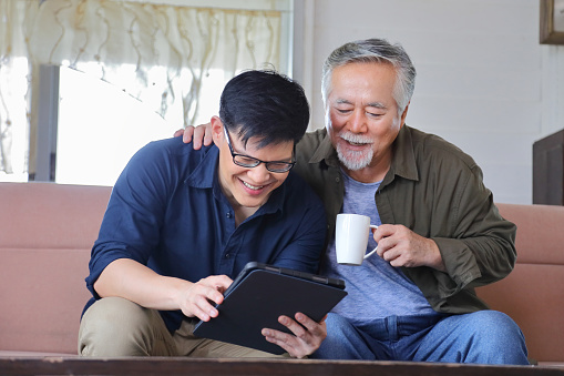 Senior Asian man in retirement age looking at photo of product available online in his son digital tablet with copy space