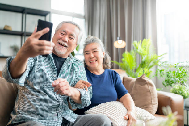 happiness asian old senior retired couple enjoy videocall to family together on sofa in living room at home,asian people use smartphone communication to family home isolation ides concept - ipad senior adult facebook sofa imagens e fotografias de stock