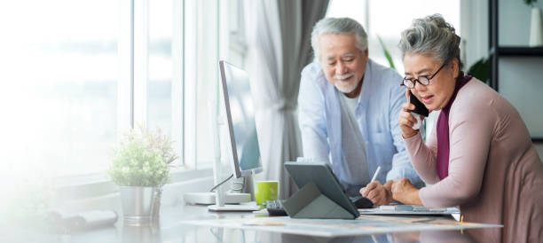 vieux seniors asiatiques retraités entrepreneur travaillant ensemble à la maison, l’isolement à domicile les emplois à distance travaillent avec un ordinateur de bureau et un smartphone technologie travail à domicile - retirement photos et images de collection