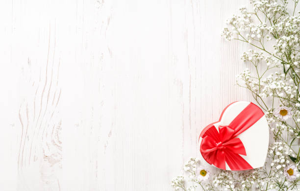 Flowers composition with gift and empty space for your text. White flowers on white wooden background and shaped heart gift. Wedding mockup with small flowers and gift with a red bow. Flat lay, top view, frame. Gypsophila Baby's-breath flowers composición de flores con regalo y espacio vacío para tu texto. flores blancas sobre fondo de madera blanca y corazón en forma de regalo. maqueta de boda con flores pequeñas y regalo con un lazo rojo. lay plano, vista superior, marco. gypsophila flores