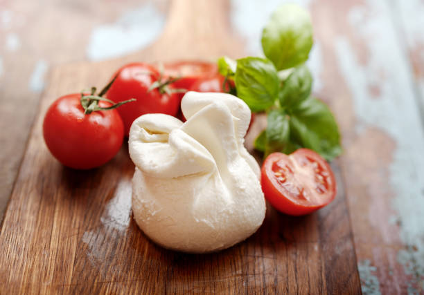 queijo burrata no tabuleiro vintage de madeira. queijo macio com tomates e folhas de manjericão na mesa de madeira. burrata saborosa com meio tomate. - buratta - fotografias e filmes do acervo