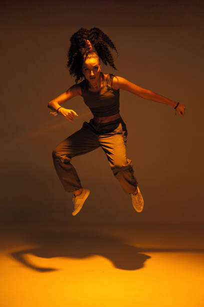 istock Dancing mixed race girl jumping and levitating in warm studio light. Female dancer performer jump in hip hop dance 1335577457