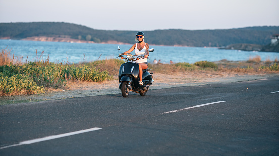 Woman wearing motorcycle helmet and traveling on motorcycle in sea road