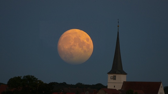 The tower of a village church in twilight with a big moon in the background