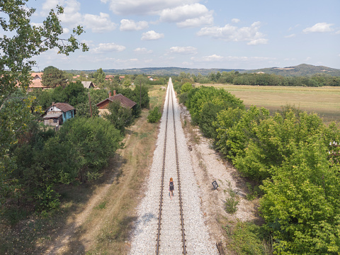 adult female traveler with backpack walking on railroad track on beautiful summer day. drone point of view