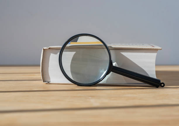istock Magnifying glass with close thick book on wood table with day light 1335649506