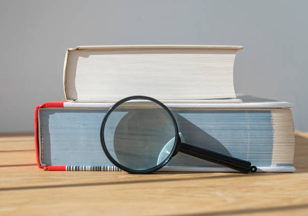 istock Magnifying glass with stack of close thick books on wooden table with day light 1335656195