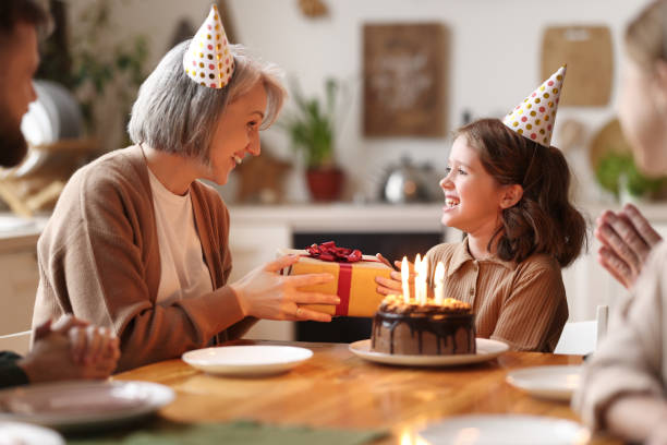 amorevole donna anziana che dà dono alla nipote felice eccitata durante la celebrazione del compleanno con la famiglia, - birthday present foto e immagini stock