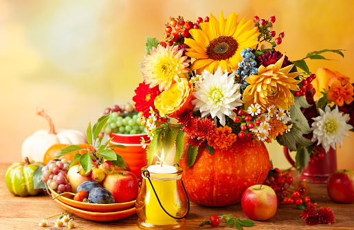 Concept of autumn festive decoration for Thanksgiving day. Autumn bouquet of flowers and berries in a pumpkin on a table, different fruits and pumpkins.