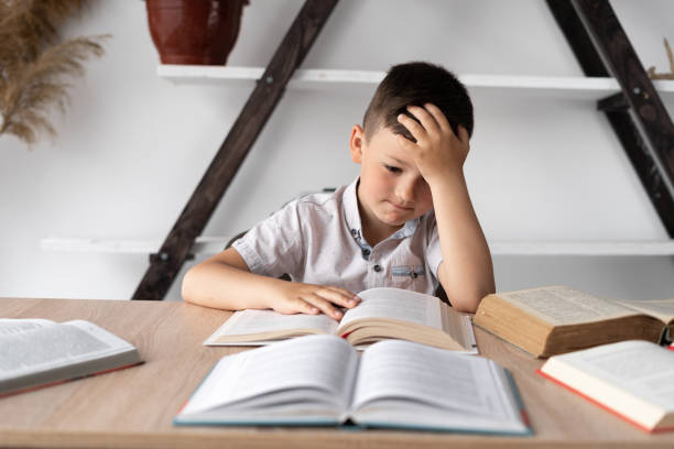 istock unmotivated student with headache sitting at home at his desk doing homework preparing for the lesson. Tired little school student reading books learning online. distance knowledge concept 1335665830