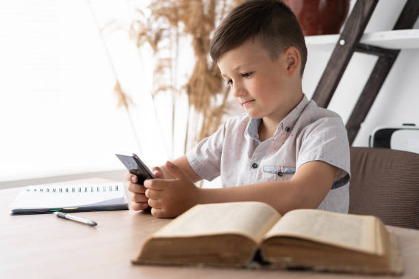 istock concentrated boy playing a game on the mobile phone while sitting at the table does homework. Gadget addicted student. Concept for online games or social network. 1335665863