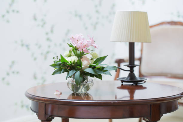 Close up flowers and the lamp on the table with sunray in the bedroom. Gray pillow on the blue bedcover.