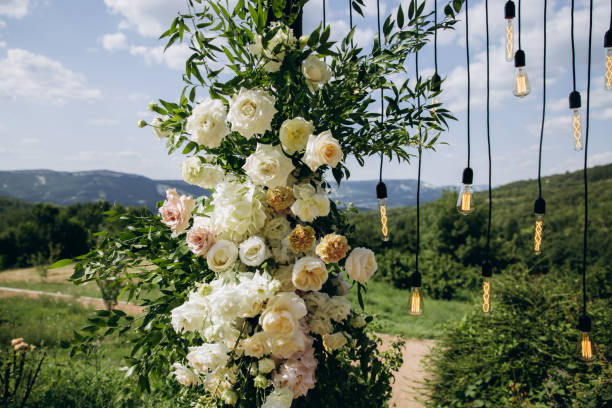 istock Wedding arch on boho style with white flowers in park with light bulbs. 1335667932