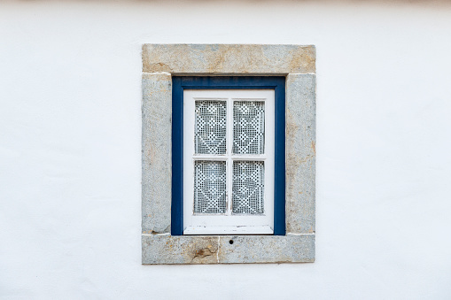 Detail of a traditional window on a white facade of a house, with crochet curtains, in Portugal.