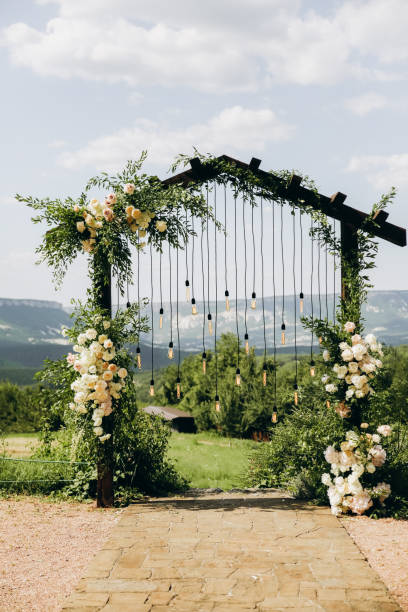 istock Wedding arch on rustuc style with white flowers in park with light bulbs. 1335669180