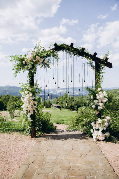 istock Wedding arch on boho style with white flowers in park with light bulbs. 1335669509