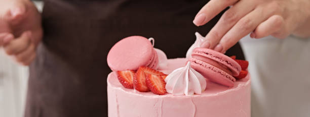 istock Woman pastry chef decorates pink cake with macaroons and berries, close-up. Cake making process, Selective focus. Banner format 1335682676