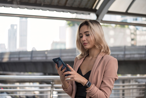 Smiling young beautiful American business woman in formal uniform check meeting schedule and chat by using corporate app on smart phone during transport in city. happy working woman with delight face.