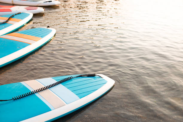 istock Surf boards on blue clean water surface background. Surfing and SUP boarding equipment in sunset lights close-up. Outdoor water sports. Surfing lifestyle concept. 1335684090