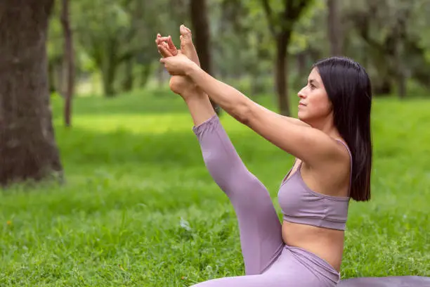 Latin woman doing Yoga-asanas with different postures, in the outdoor park with grass and trees in the background. High quality photo