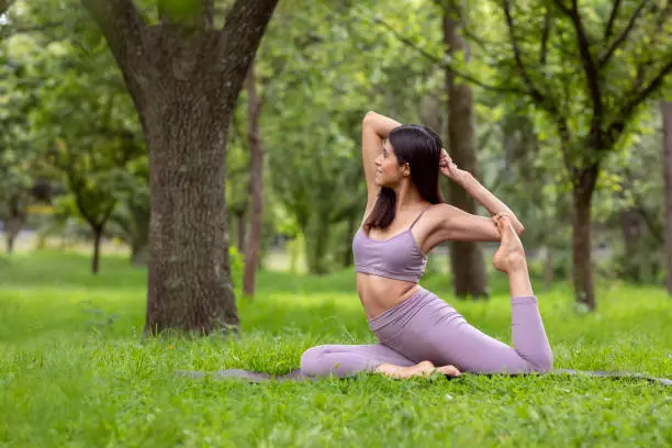Latin woman doing Yoga-asanas with different postures, in the outdoor park with grass and trees in the background. High quality photo