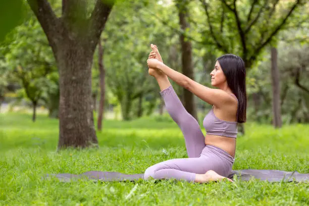 Latin woman doing Yoga-asanas with different postures, in the outdoor park with grass and trees in the background. High quality photo